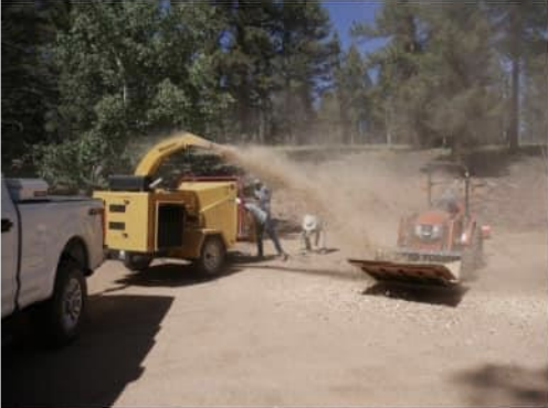 Chipper connected to the back of a pickup truck spraying chips into the bucket of a utility vehicle 